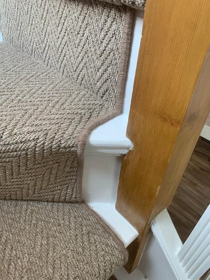 Beige herringbone weave carpet neatly fitted around stair woodwork