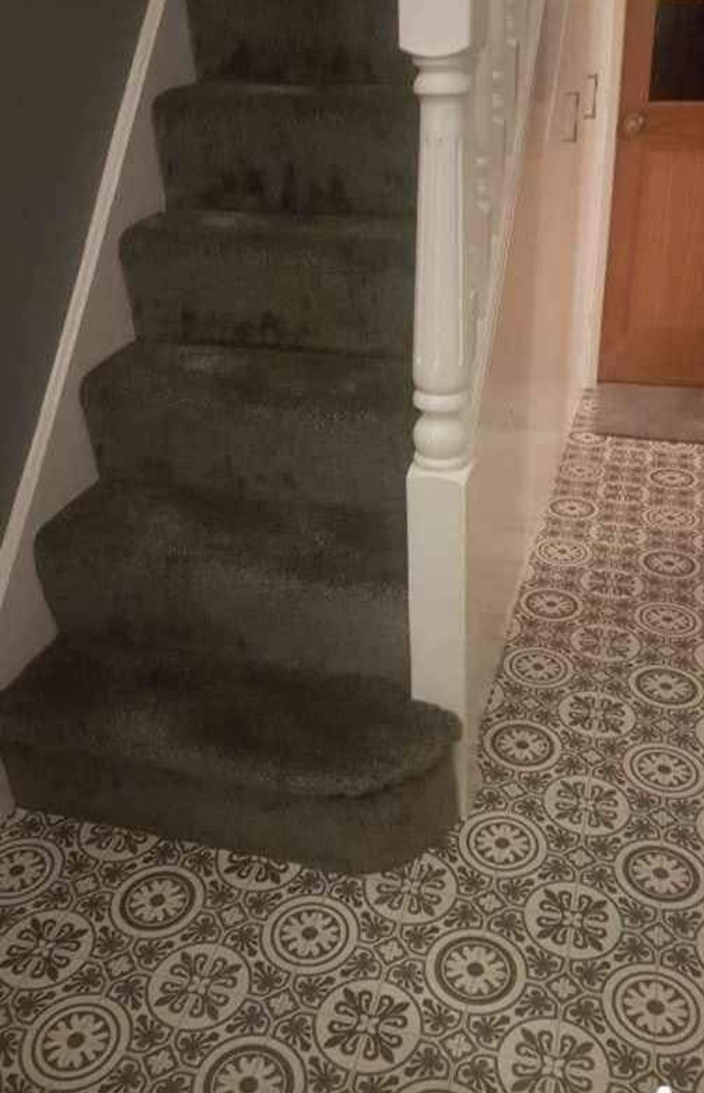 Grey carpeted stairs meeting a patterned hallway floor